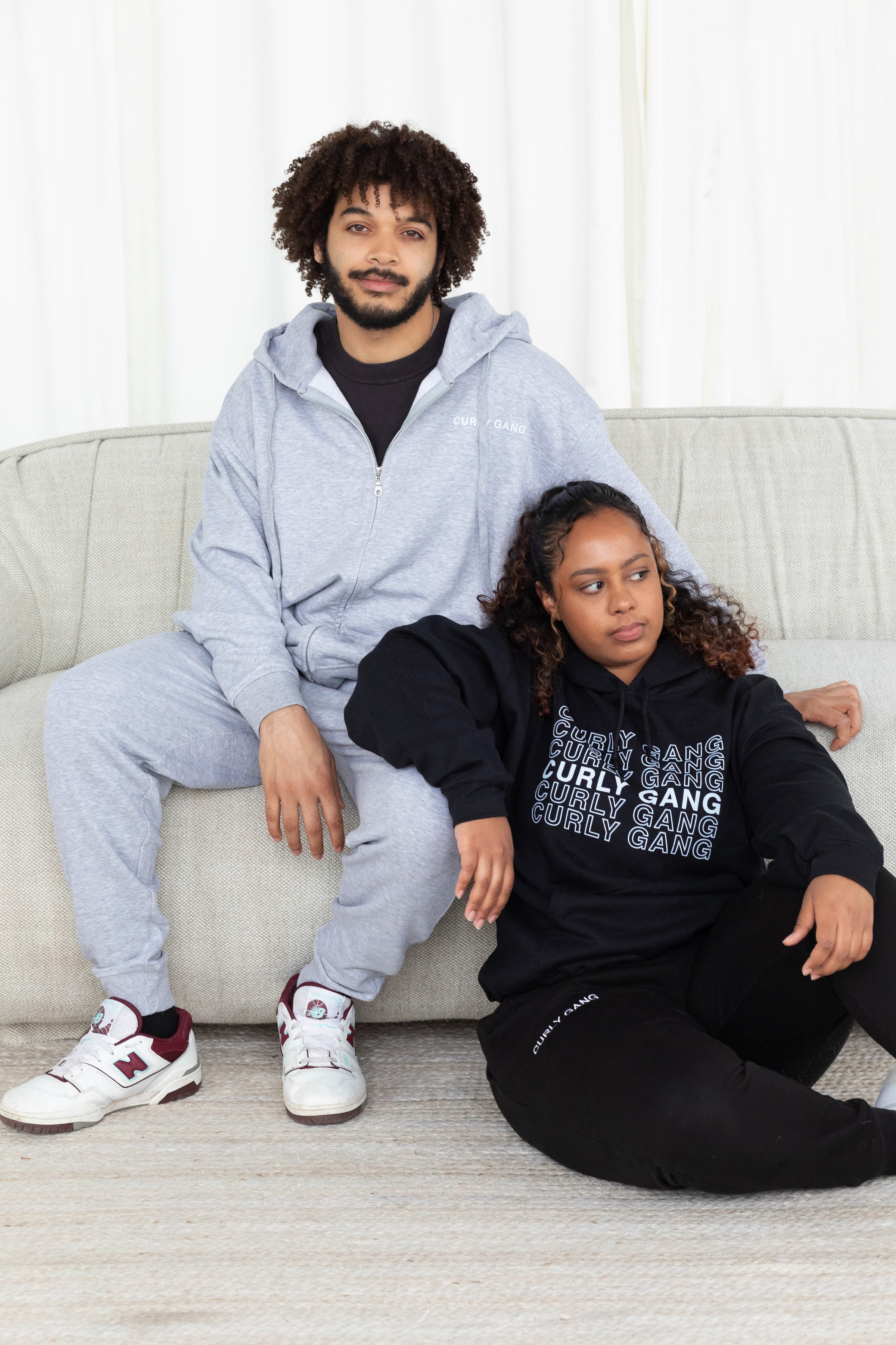 Black man and woman in curly gang zip up hoodie in grey, curly gang hoodie in black and the curly gang sweatpants